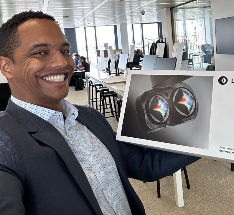 Photo of Sikaar smiling and holding a box with VR headset Lynx Mixed Reality in an office setting, showcasing his involvement in AR/VR technology.